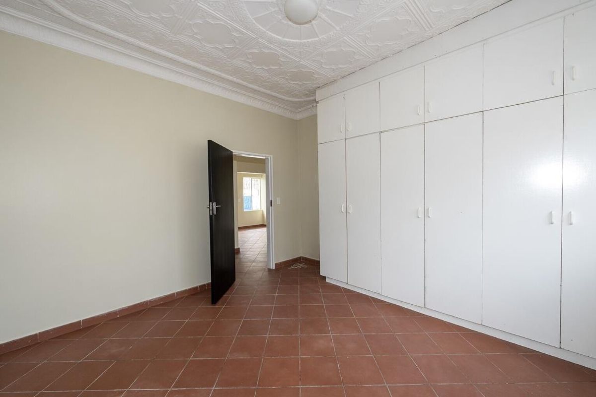 A spacious bedroom featuring extensive built-in floor-to-ceiling cabinetry, decorative pressed metal ceiling, and terracotta-style tiled flooring.