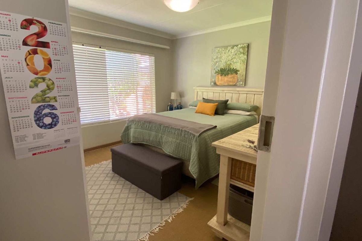 A cozy bedroom featuring neutral wall tones, a large window with fitted blinds, and a central ceiling light fixture.
