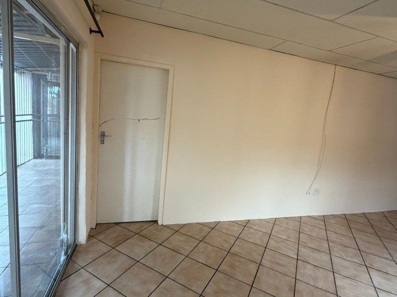 An empty living area featuring tiled flooring, a sliding glass door, and a drop ceiling, requiring cosmetic updates and repairs.