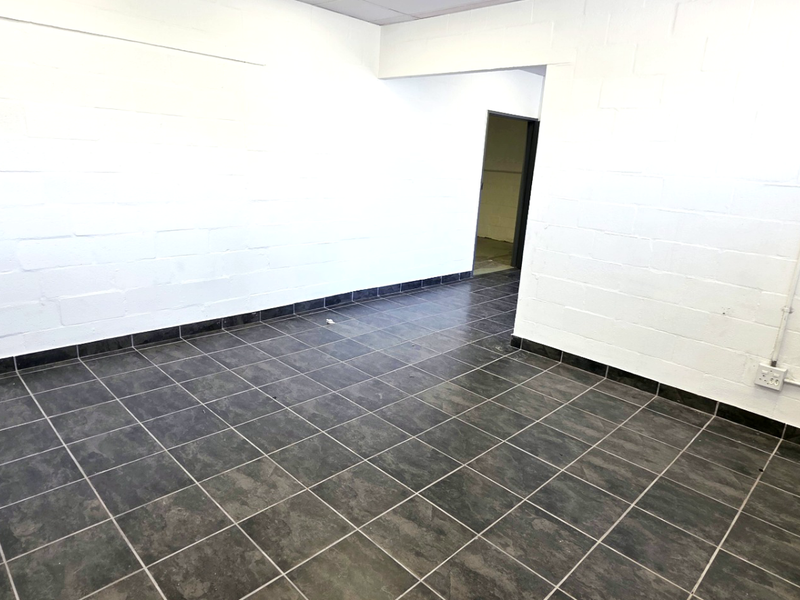 A clean, empty utility or office space featuring durable tiled flooring and painted concrete block walls with exposed electrical conduit.