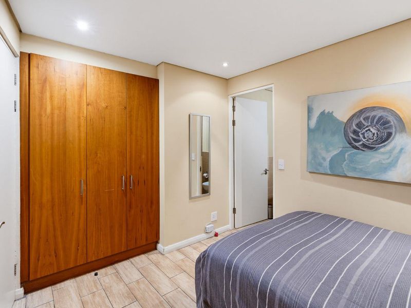 A well-maintained bedroom featuring built-in wooden wardrobes, tiled flooring, and recessed downlighting, with an adjacent en-suite bathroom access.