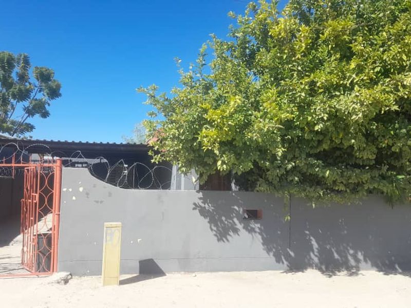 Front exterior view of the property featuring a perimeter wall with razor wire, a metal entrance gate, and a covered carport area.
