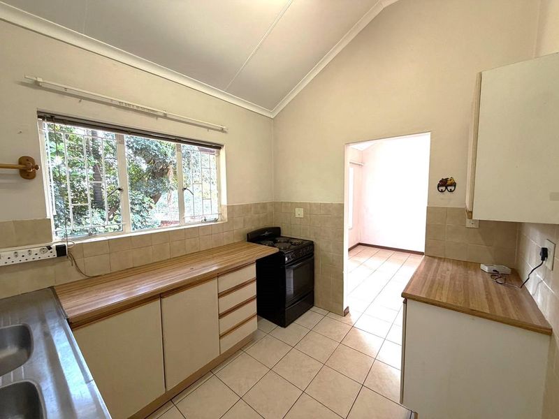 A functional kitchen featuring laminate countertops, tiled backsplash, and a freestanding stove, with ceramic floor tiles and built-in cabinetry.