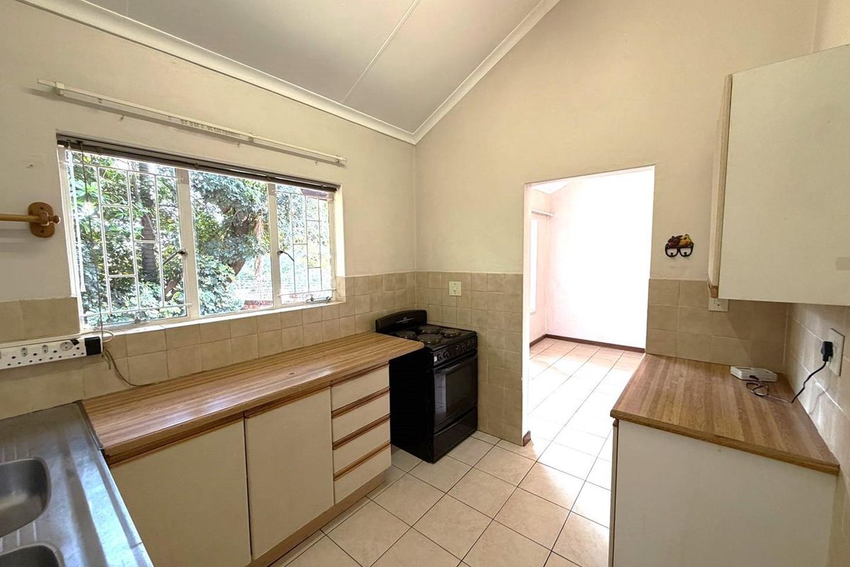 A functional kitchen featuring laminate countertops, tiled backsplash, and a freestanding stove, with ceramic floor tiles and built-in cabinetry.
