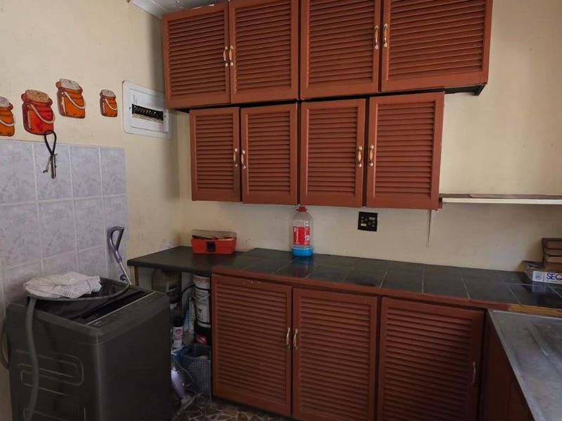 A functional laundry area featuring louvered cabinetry, tiled countertops, and a stainless steel sink, offering practical utility space with potential for modernization.