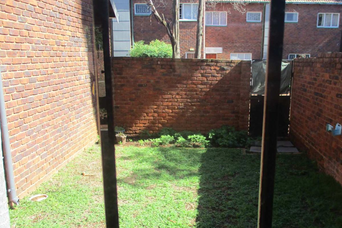 A private rear courtyard area featuring a small lawn enclosed by brick boundary walls and a rear access gate.