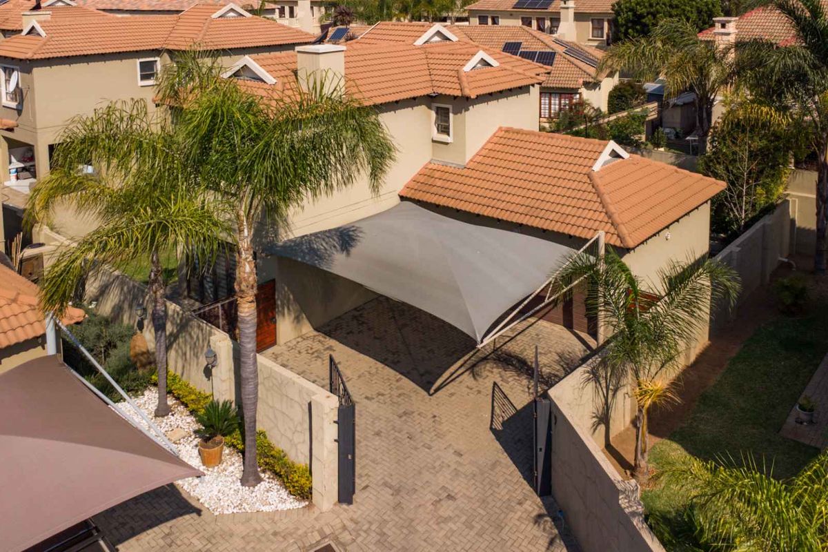 Aerial view of a residential property featuring a paved driveway, shade sail, and terracotta tiled roof within a secure estate setting.