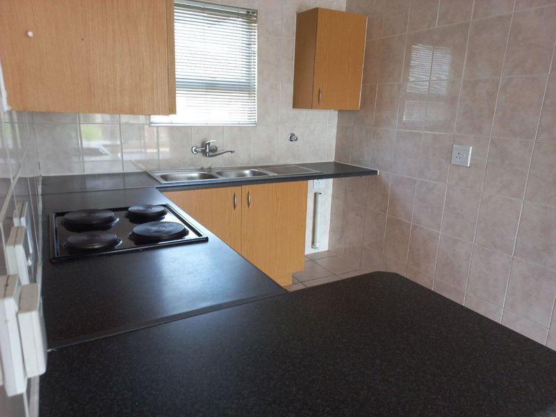 A functional kitchen featuring laminate cabinetry, dark countertops, an integrated electric hob, and a stainless steel double sink with tiled splashbacks.