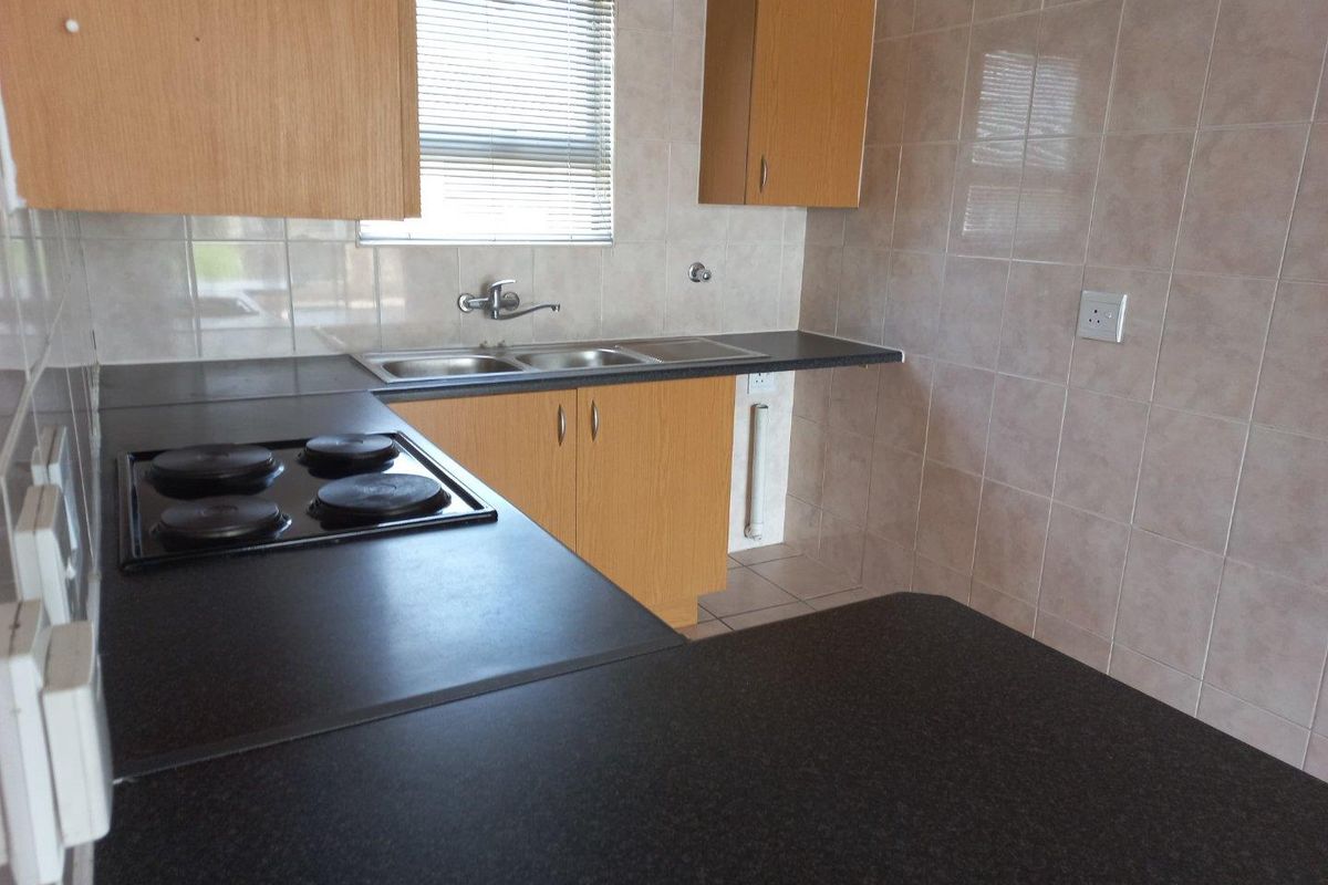 A functional kitchen featuring laminate cabinetry, dark countertops, an integrated electric hob, and a stainless steel double sink with tiled splashbacks.