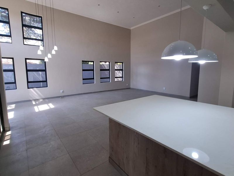 Spacious open-plan living area featuring double-volume ceilings, modern tiled flooring, and a central kitchen island with stone countertops and contemporary pendant lighting.