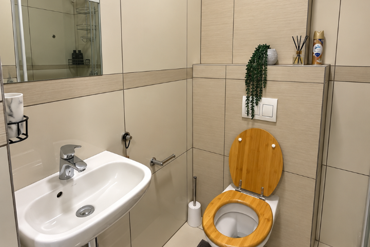 Modern bathroom featuring a wall-mounted toilet with a wooden seat, a sleek wall-mounted basin, and neutral large-format tiling throughout.