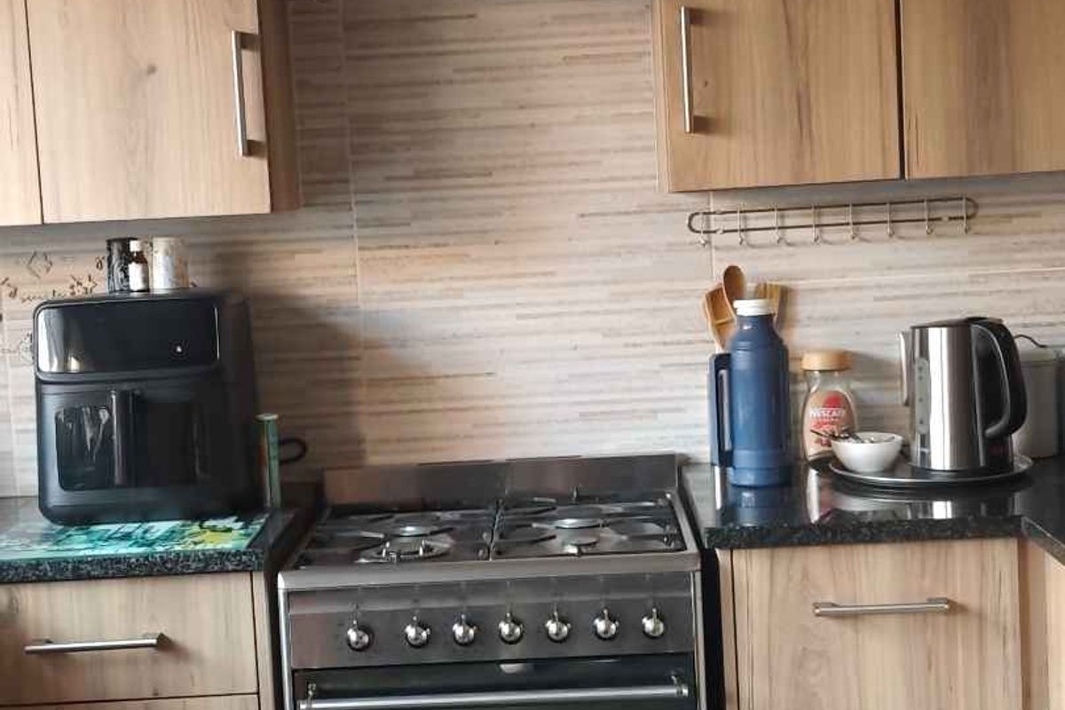A functional kitchen featuring wood-look cabinetry, a gas stove with oven, and a tiled backsplash with granite countertops.