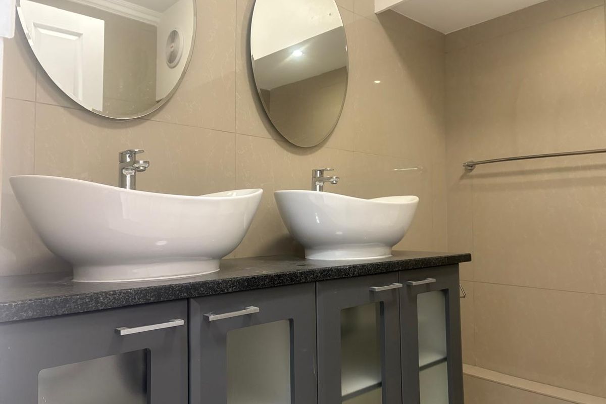 Modern bathroom featuring a double vanity with vessel sinks, dark cabinetry, and large format beige wall tiles.