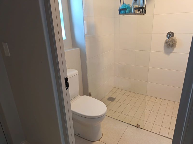 A clean and modern bathroom featuring a walk-in shower with a glass screen, white wall tiles, and a standard toilet.