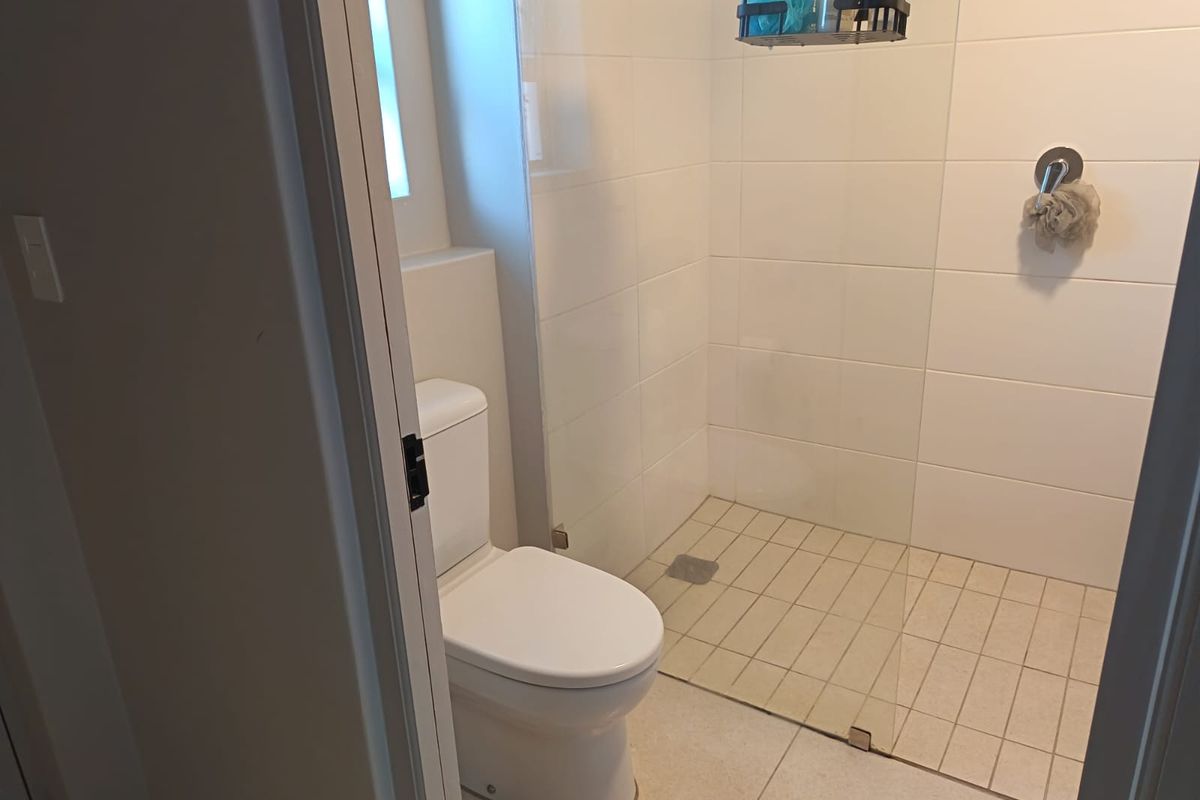 A clean and modern bathroom featuring a walk-in shower with a glass screen, white wall tiles, and a standard toilet.