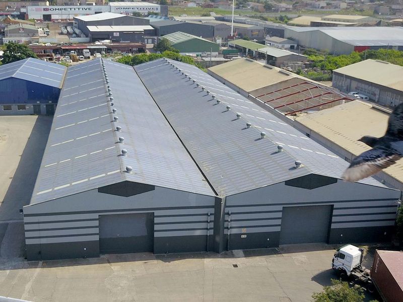 Aerial view of a large industrial warehouse complex featuring dual pitched metal roofing, roller shutter doors, and paved yard space.