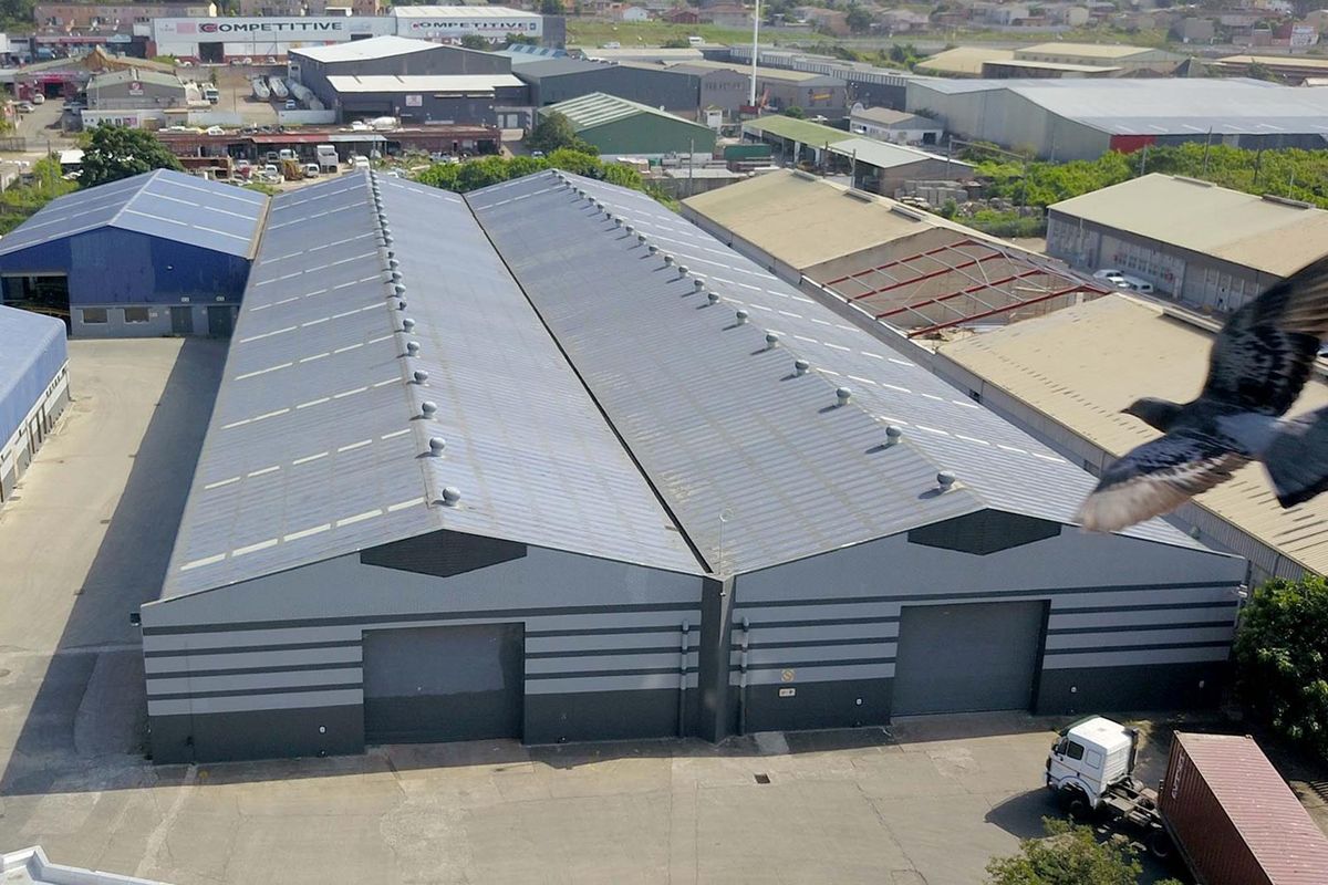 Aerial view of a large industrial warehouse complex featuring dual pitched metal roofing, roller shutter doors, and paved yard space.