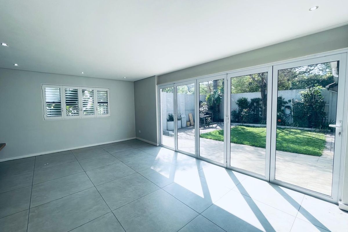 Spacious, light-filled living area featuring large format floor tiles, recessed downlights, and expansive aluminium stacker doors opening onto a private garden.