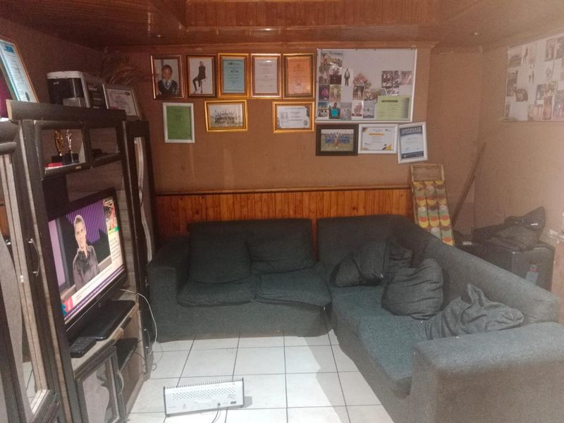 A living room featuring wooden ceiling and wall paneling with ceramic floor tiles, offering a dated aesthetic that could benefit from modern updates.