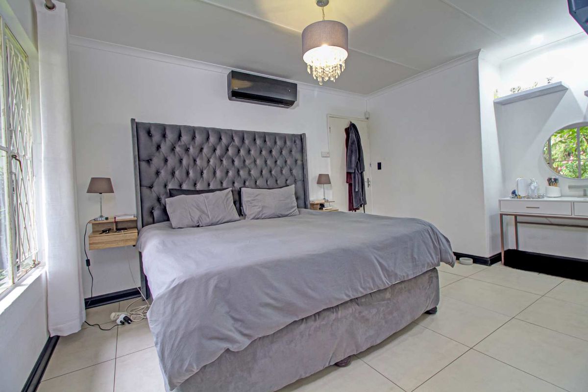 A well-maintained bedroom featuring tiled flooring, a wall-mounted air conditioning unit, and a neutral color palette.