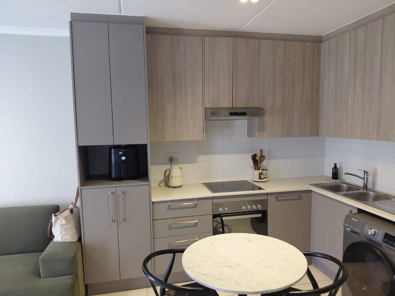 Modern kitchen featuring light wood and grey cabinetry, stone countertops, integrated appliances, and a tiled backsplash in a compact, functional layout.