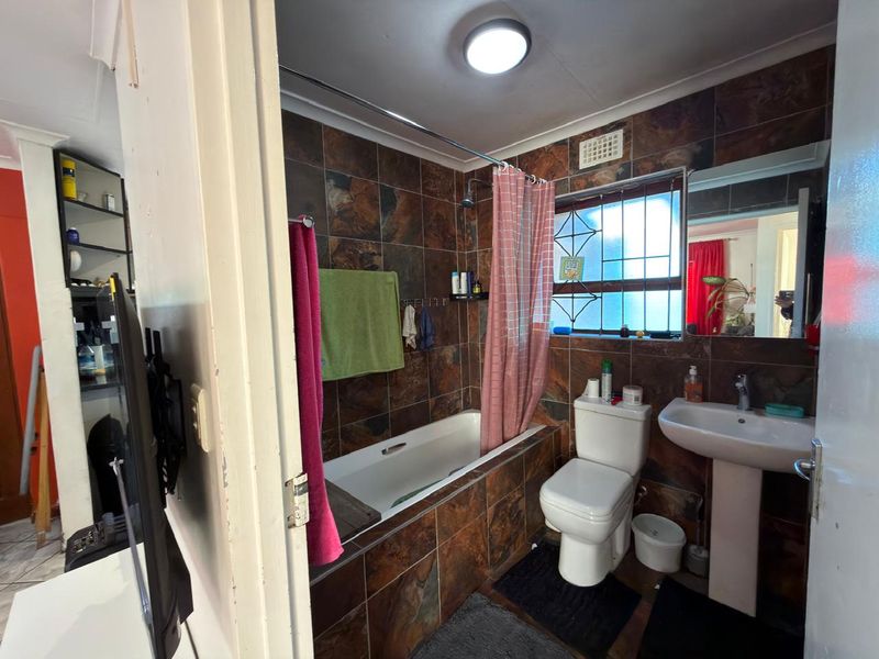 A compact bathroom featuring a bathtub with shower attachment, pedestal sink, and toilet, finished with dark, dated wall tiles.