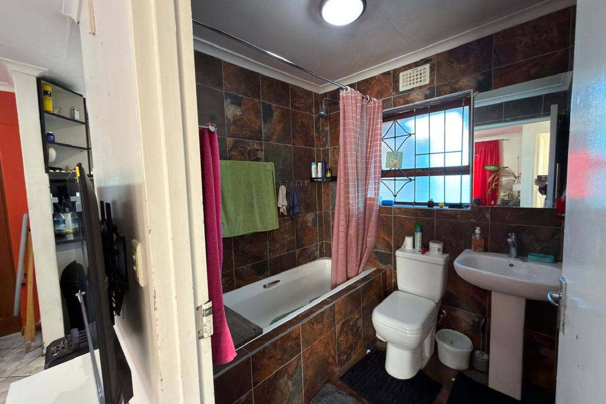 A compact bathroom featuring a bathtub with shower attachment, pedestal sink, and toilet, finished with dark, dated wall tiles.