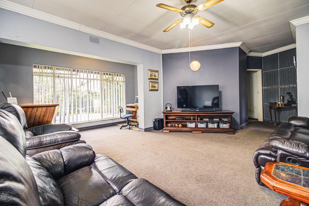 Spacious living room featuring neutral wall tones, large windows with vertical blinds, and a ceiling fan, offering a comfortable and functional family living space.