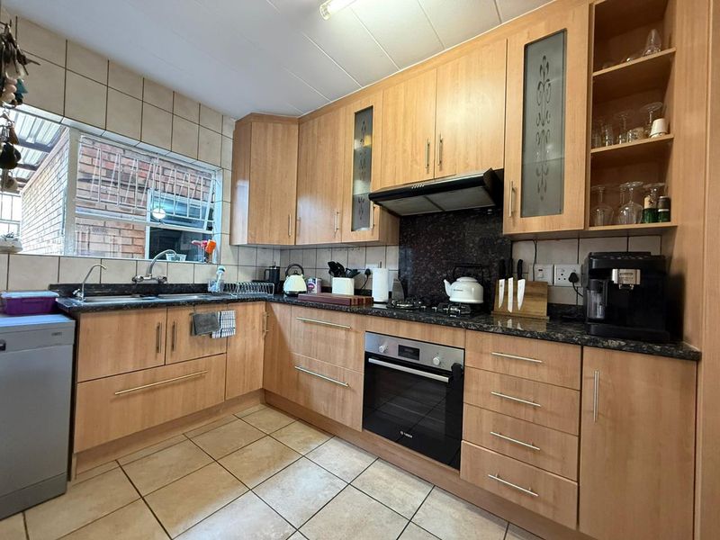 A functional kitchen featuring light wood cabinetry, granite countertops, a built-in oven with gas hob, and tiled flooring.