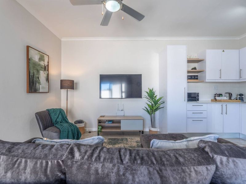 An open-plan living area featuring a compact kitchen with white cabinetry and a ceiling fan, creating a functional and cohesive living space.