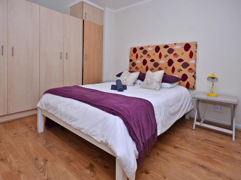 A well-maintained bedroom featuring light wood-tone laminate flooring and ample built-in cupboard storage space.