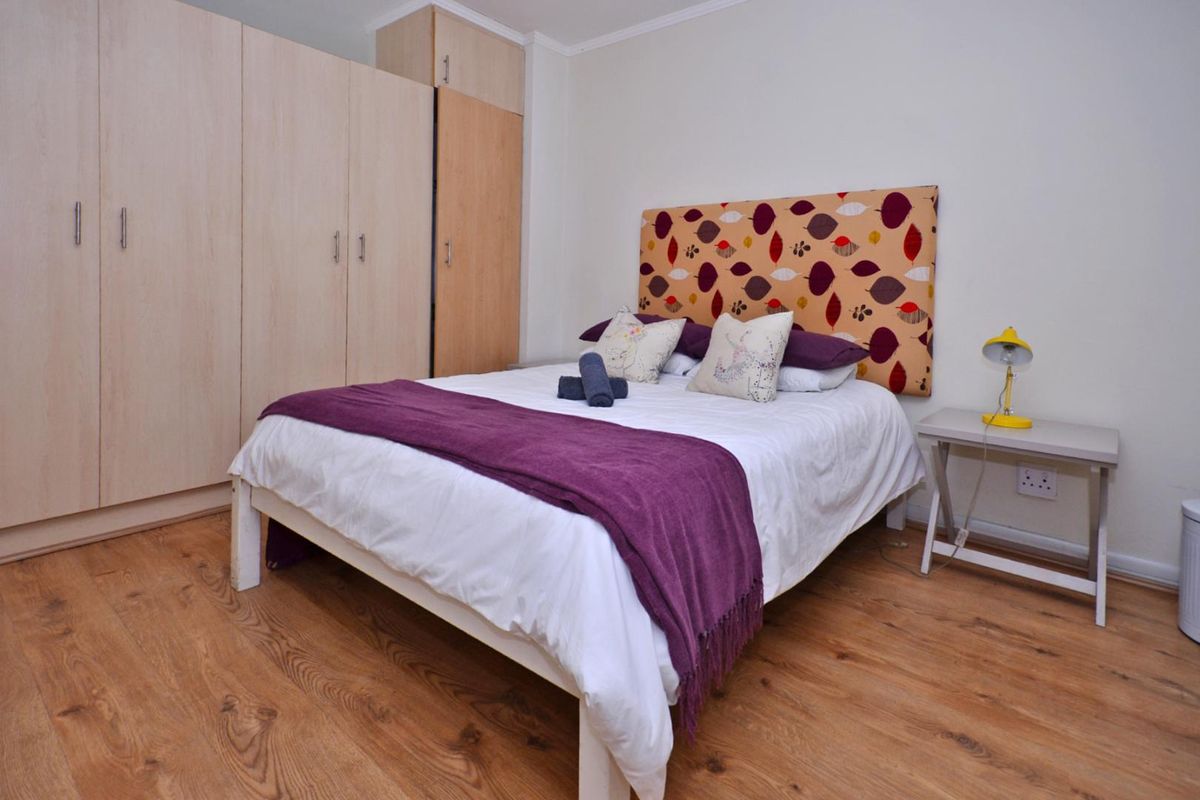 A well-maintained bedroom featuring light wood-tone laminate flooring and ample built-in cupboard storage space.