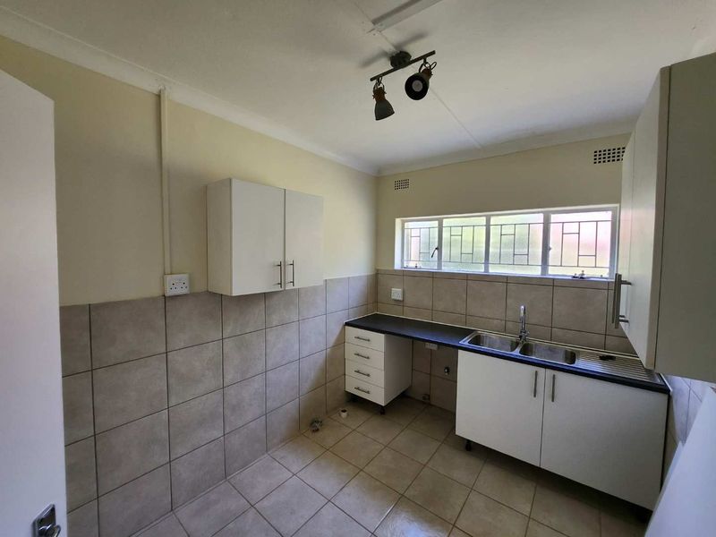 A functional, empty kitchen featuring tiled splashbacks, double basin sink, laminate countertops, and ample built-in cabinetry with neutral finishes.