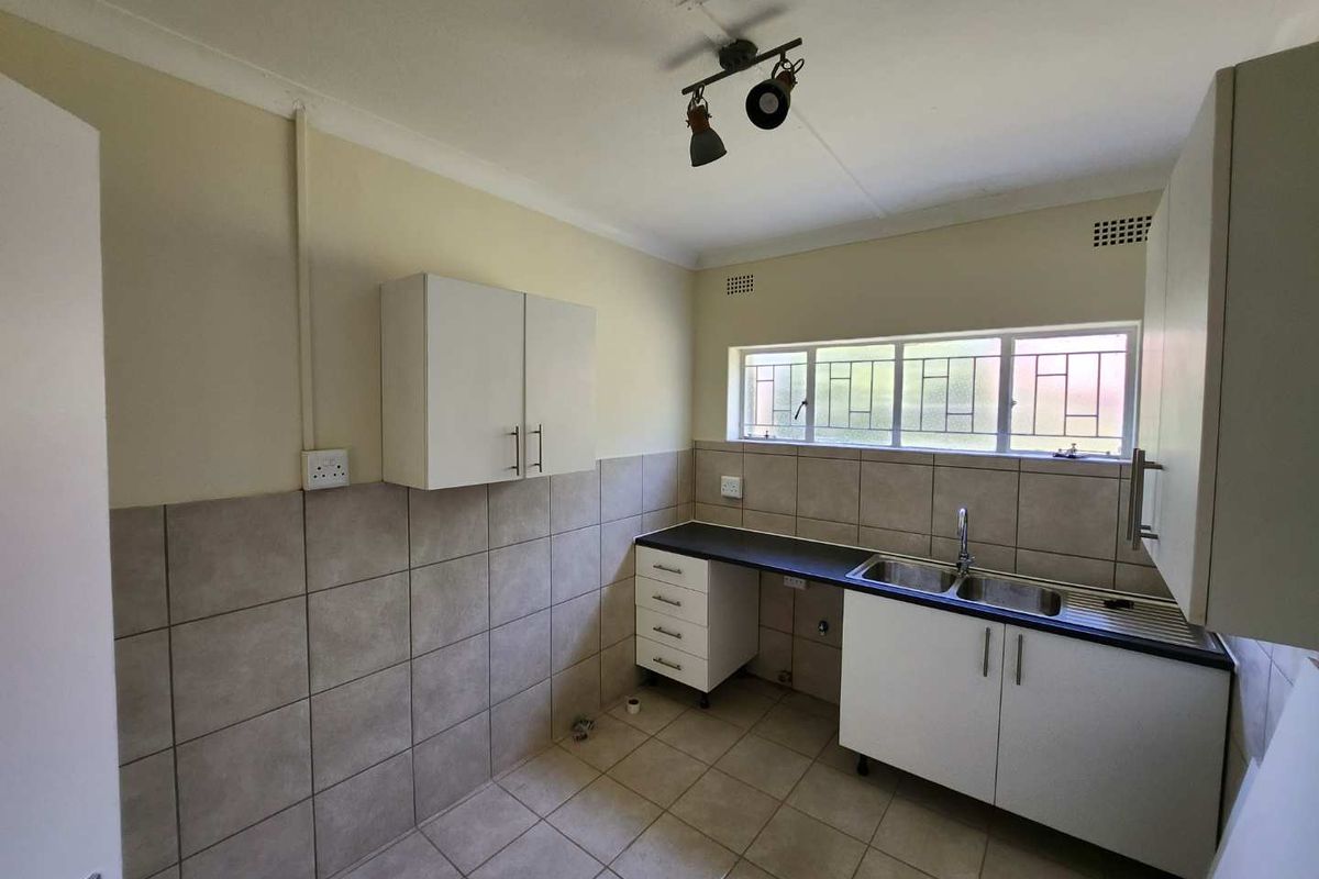 A functional, empty kitchen featuring tiled splashbacks, double basin sink, laminate countertops, and ample built-in cabinetry with neutral finishes.