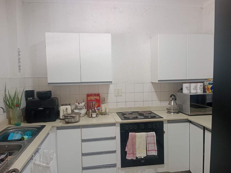 A compact kitchen featuring white cabinetry, laminate countertops, a tiled backsplash, and integrated electric cooking appliances.