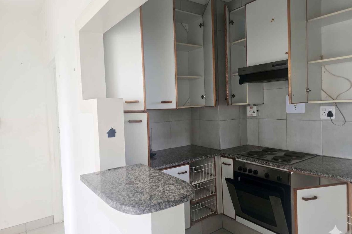 Compact kitchen featuring granite countertops, built-in oven, electric hob, extractor fan, and tiled flooring with a breakfast nook counter.