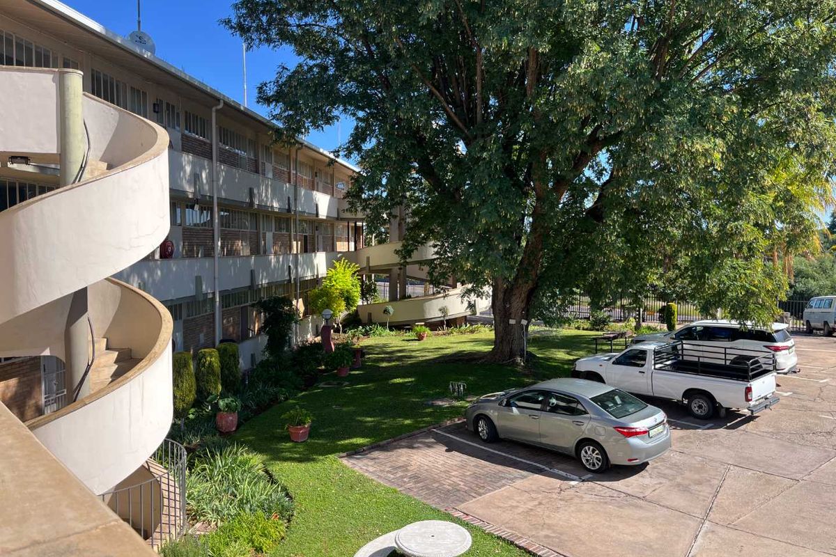 Exterior view of an apartment complex featuring a spiral staircase, landscaped garden area, and paved parking facilities.