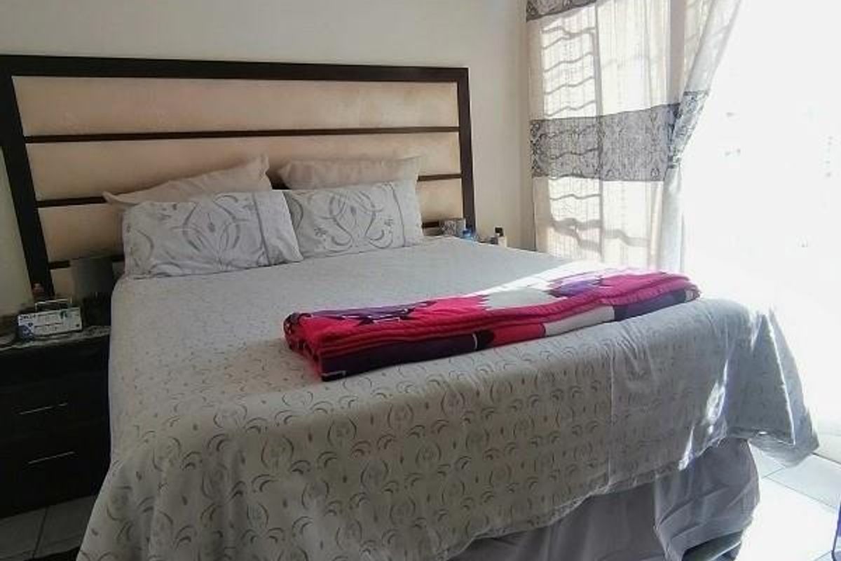 A bedroom featuring tiled flooring and large windows with curtains, providing natural light and access to an outdoor area.