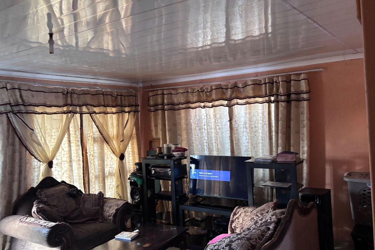 A living room featuring a glossy panelled ceiling and large windows with layered curtains, providing a functional space for relaxation.