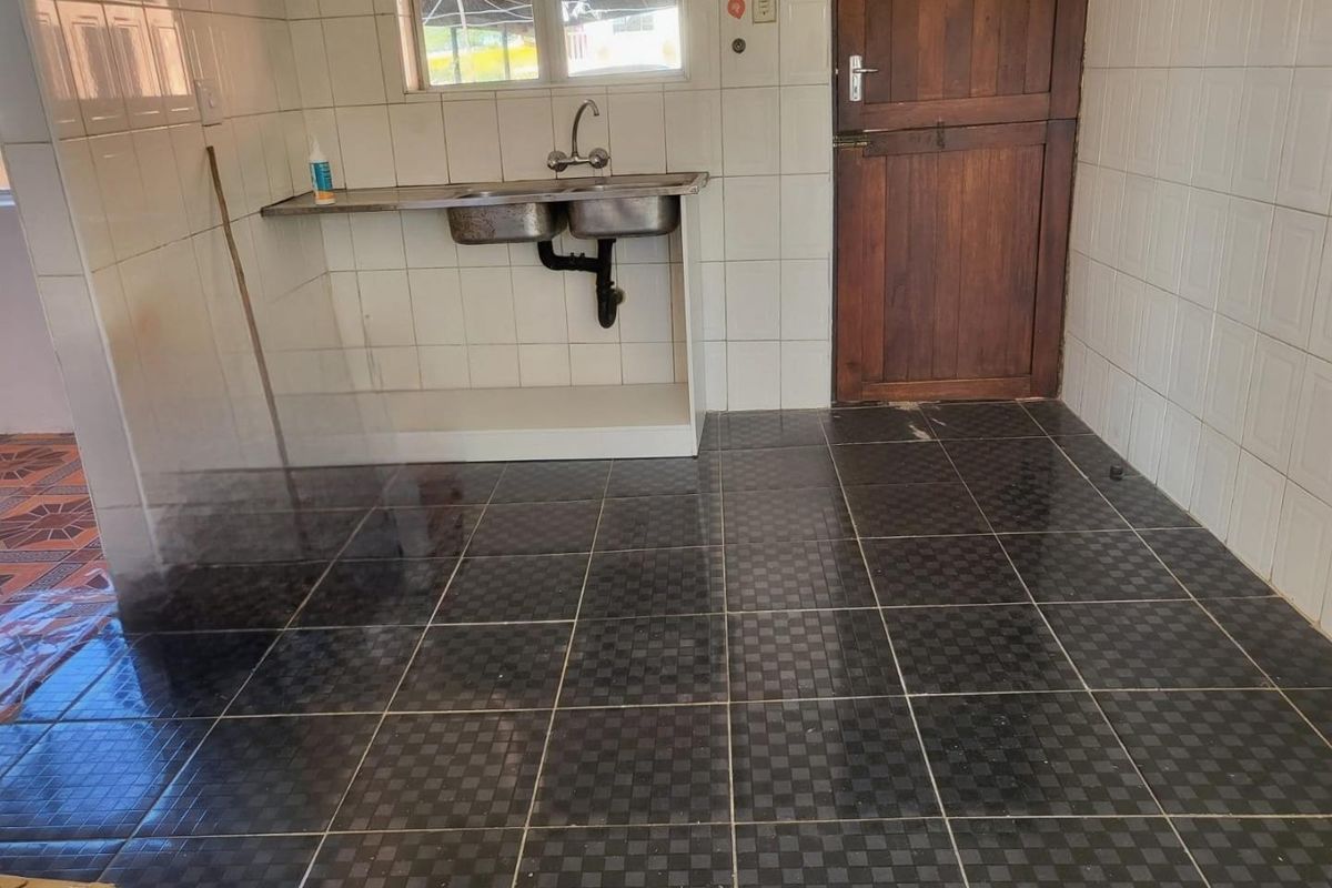 A basic kitchen area featuring tiled walls, dark checkered floor tiles, a stainless steel double sink, and a timber door.