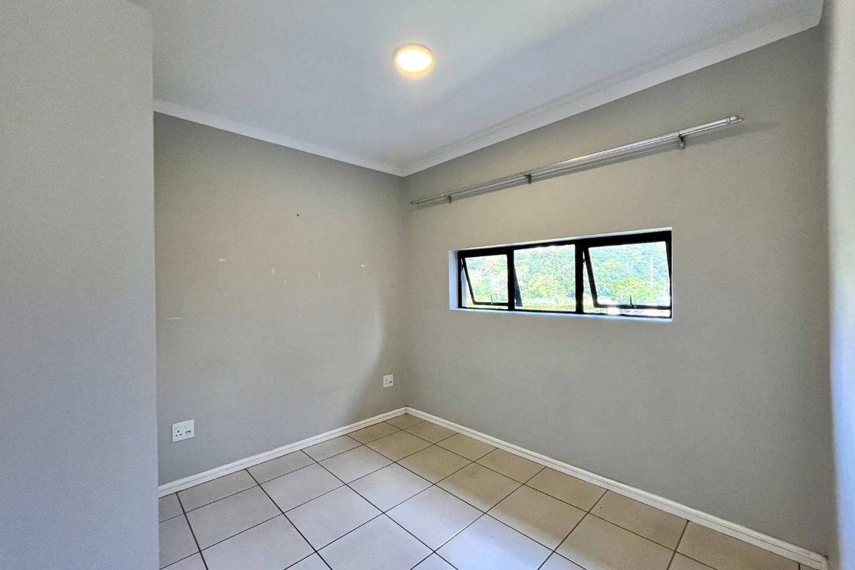 A clean, empty bedroom featuring neutral tiled flooring, a top-hung window with a curtain rod, and simple wall finishes.