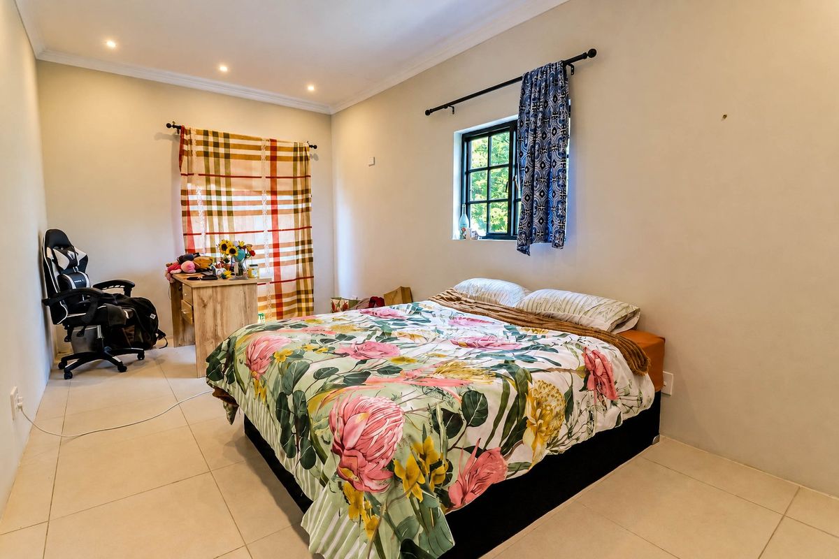 A bedroom featuring tiled flooring, recessed downlighting, and a window with a black frame, providing a functional and well-lit living space.