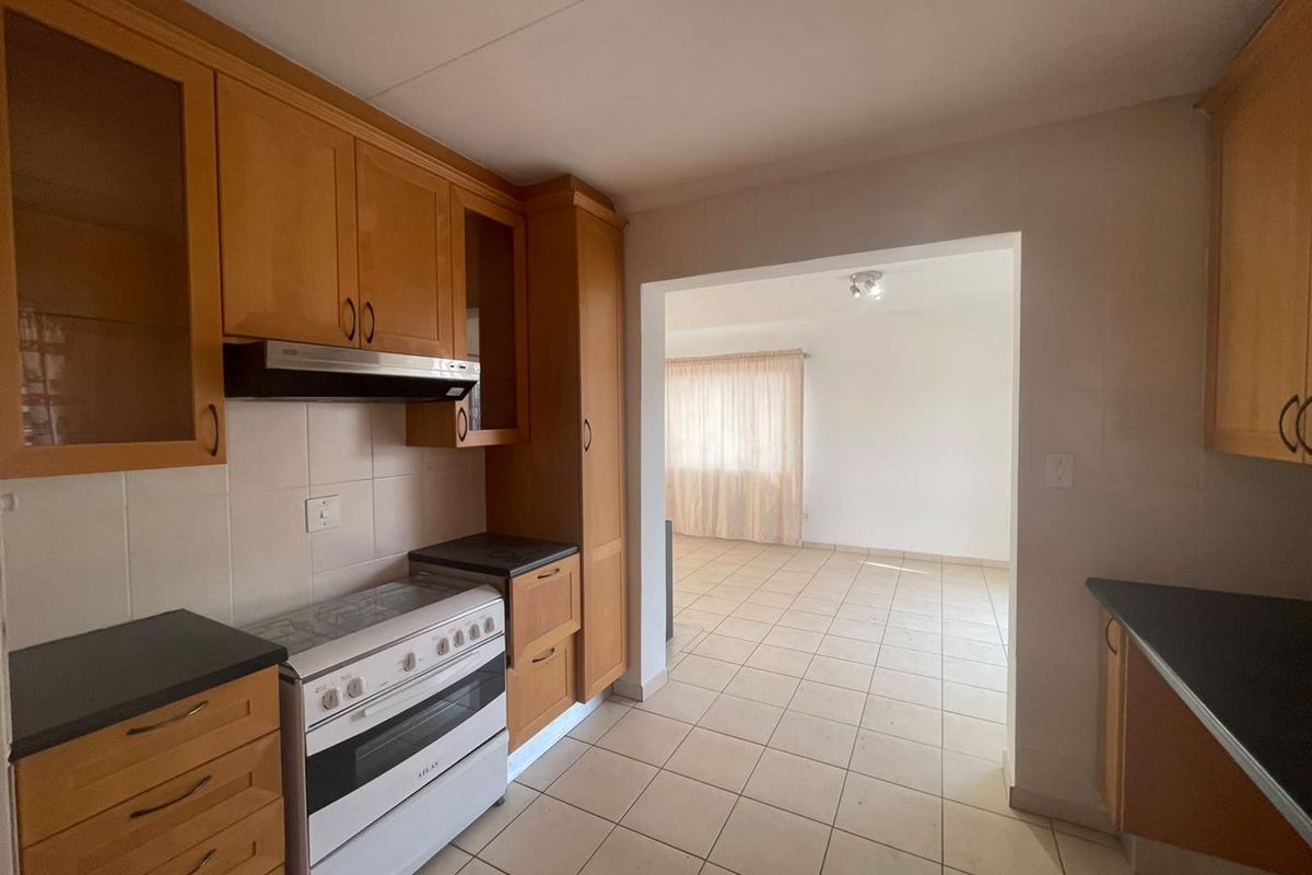 A functional kitchen featuring wooden cabinetry, a freestanding stove with extractor fan, and tiled flooring, leading into an adjacent living area.