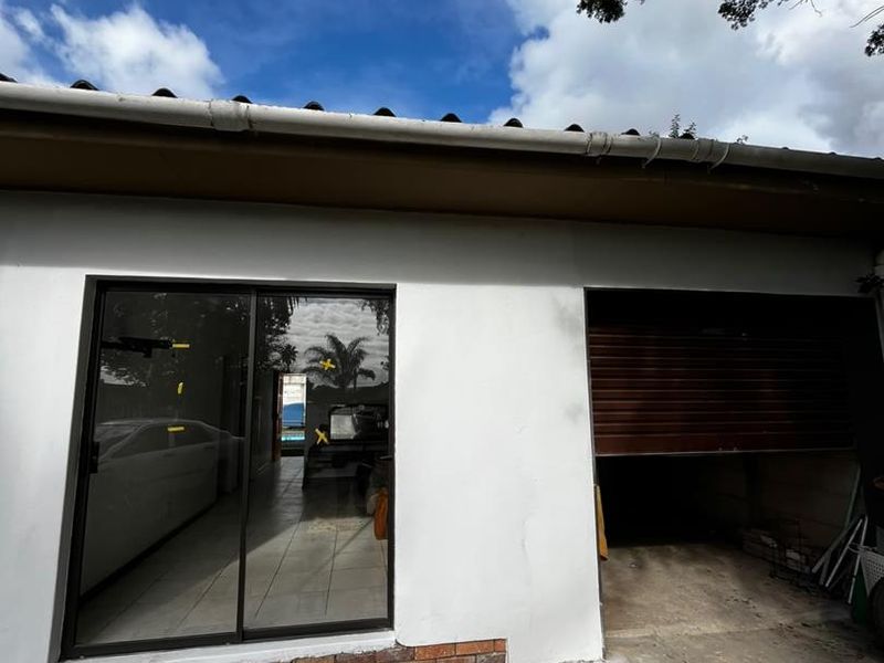 Rear exterior view of the cottage featuring a sliding glass door, a roller garage door, and a concrete driveway with visible surface cracking.