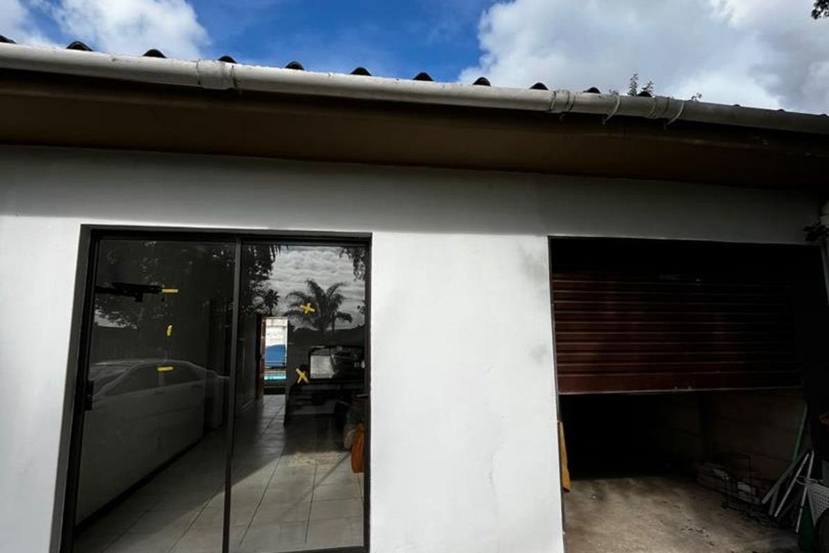 Rear exterior view of the cottage featuring a sliding glass door, a roller garage door, and a concrete driveway with visible surface cracking.