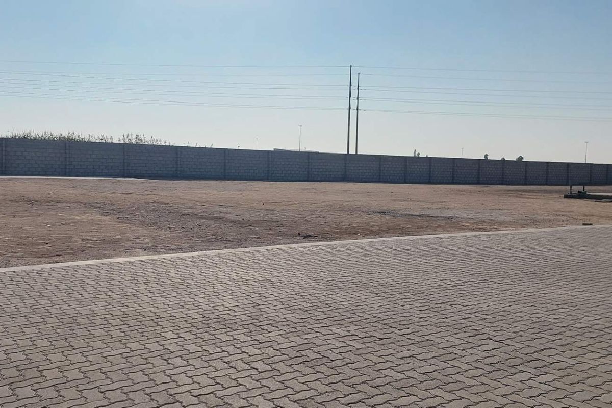 A large, open industrial yard featuring extensive paving, a perimeter boundary wall, and a concrete slab area suitable for storage or logistics.