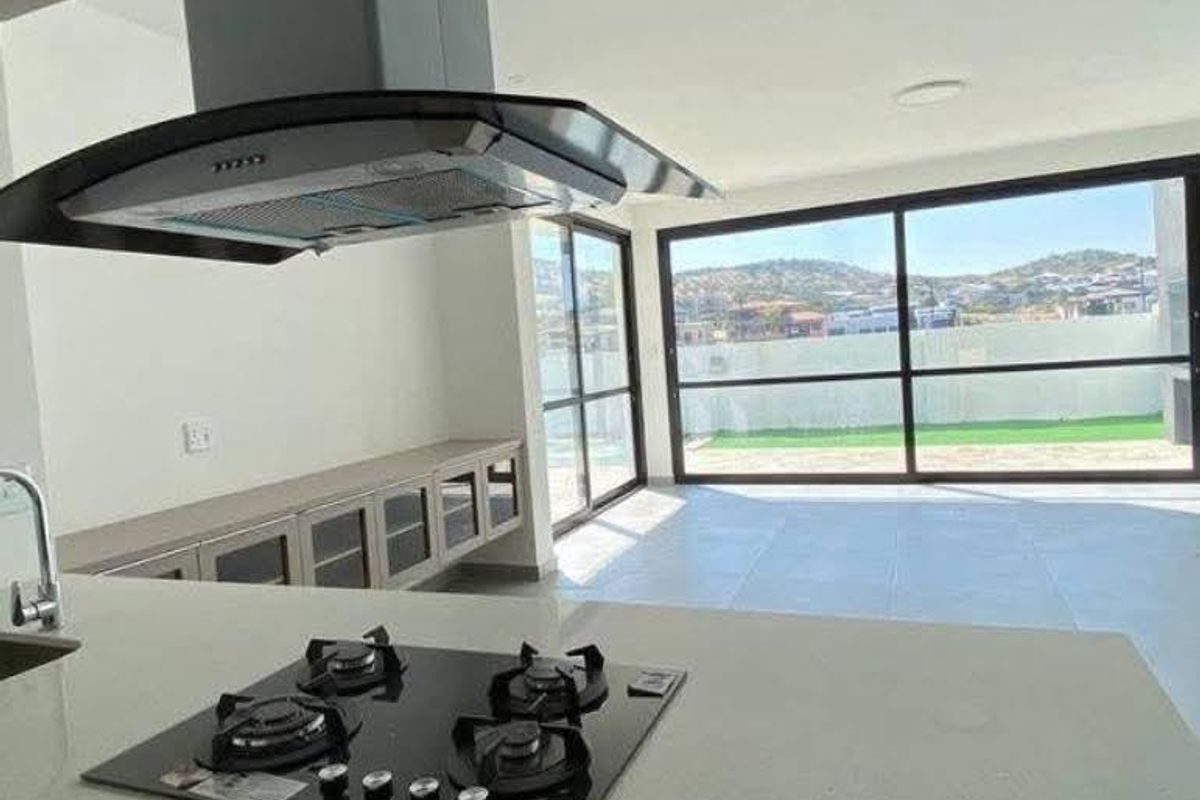 Modern open-plan kitchen featuring stone countertops, gas hob, and extractor fan, flowing into a bright living area with large sliding doors to the garden.