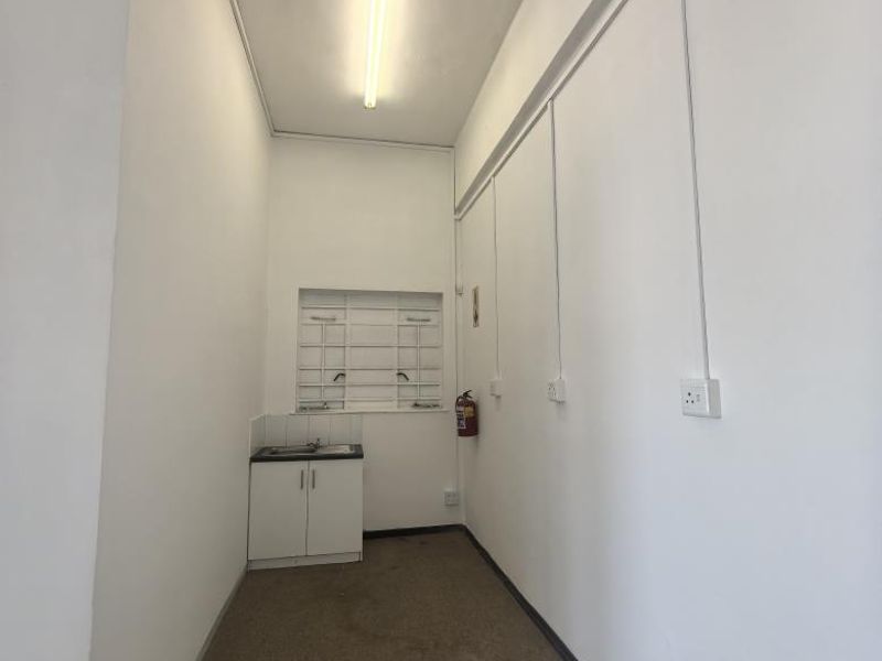 A compact utility or scullery area featuring a small built-in sink cabinet, fluorescent lighting, and security bars on the window.