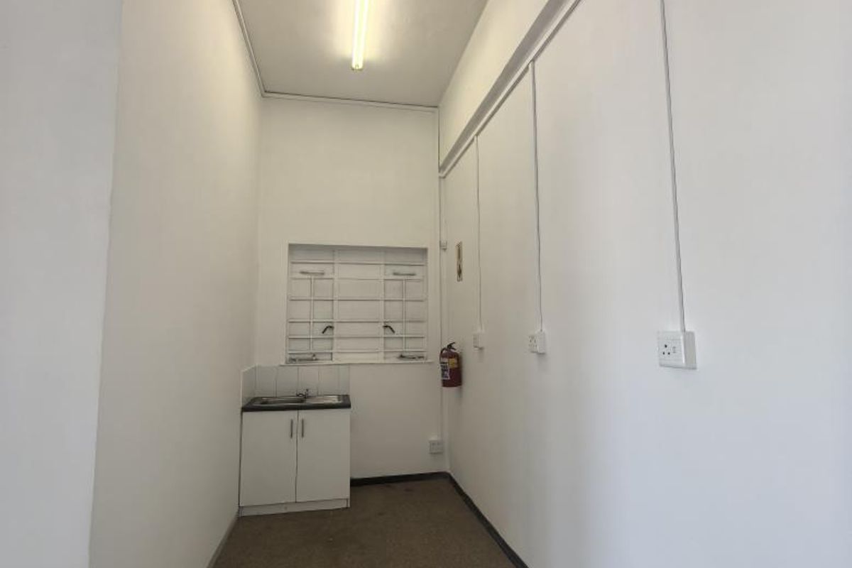 A compact utility or scullery area featuring a small built-in sink cabinet, fluorescent lighting, and security bars on the window.