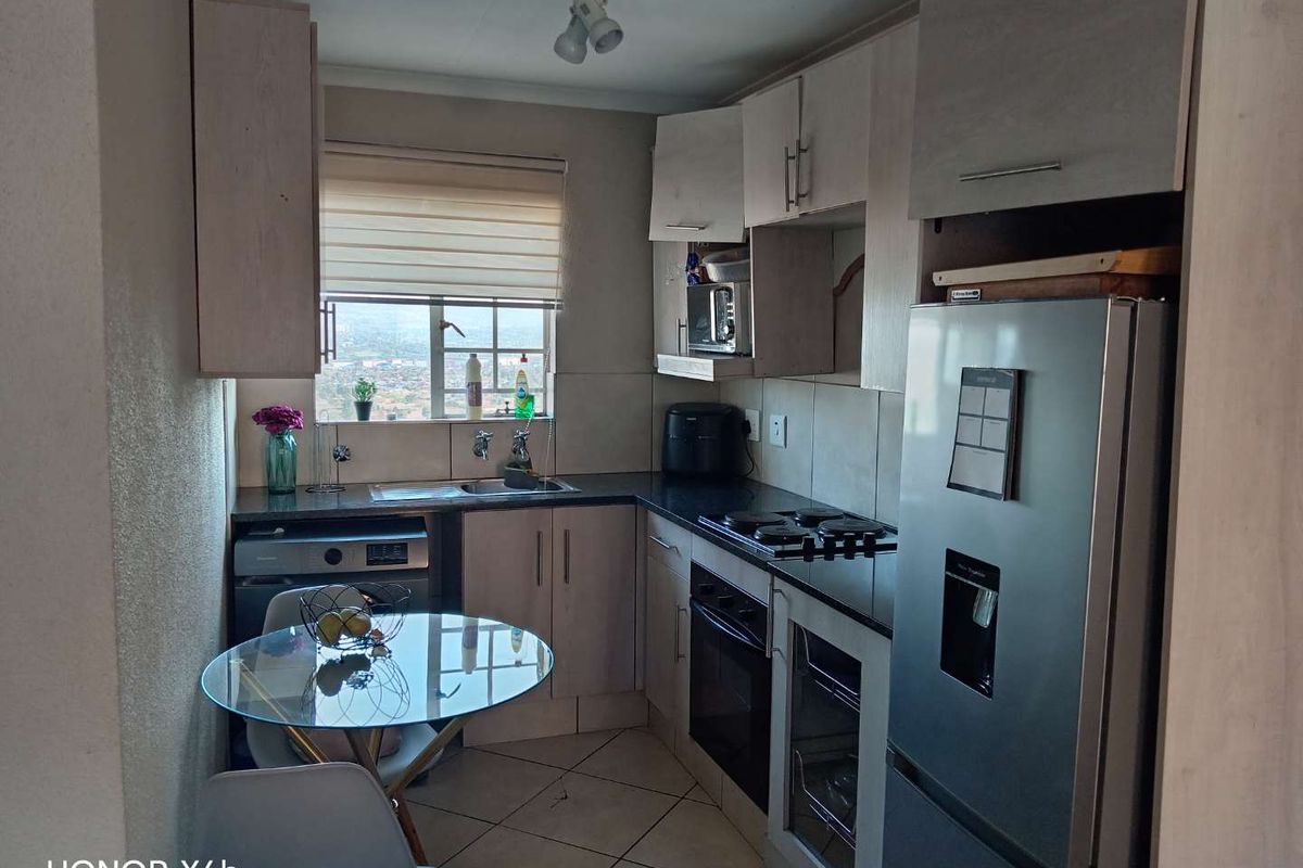 Compact kitchen featuring built-in cabinetry, granite countertops, integrated oven and hob, and tiled flooring with a window view.